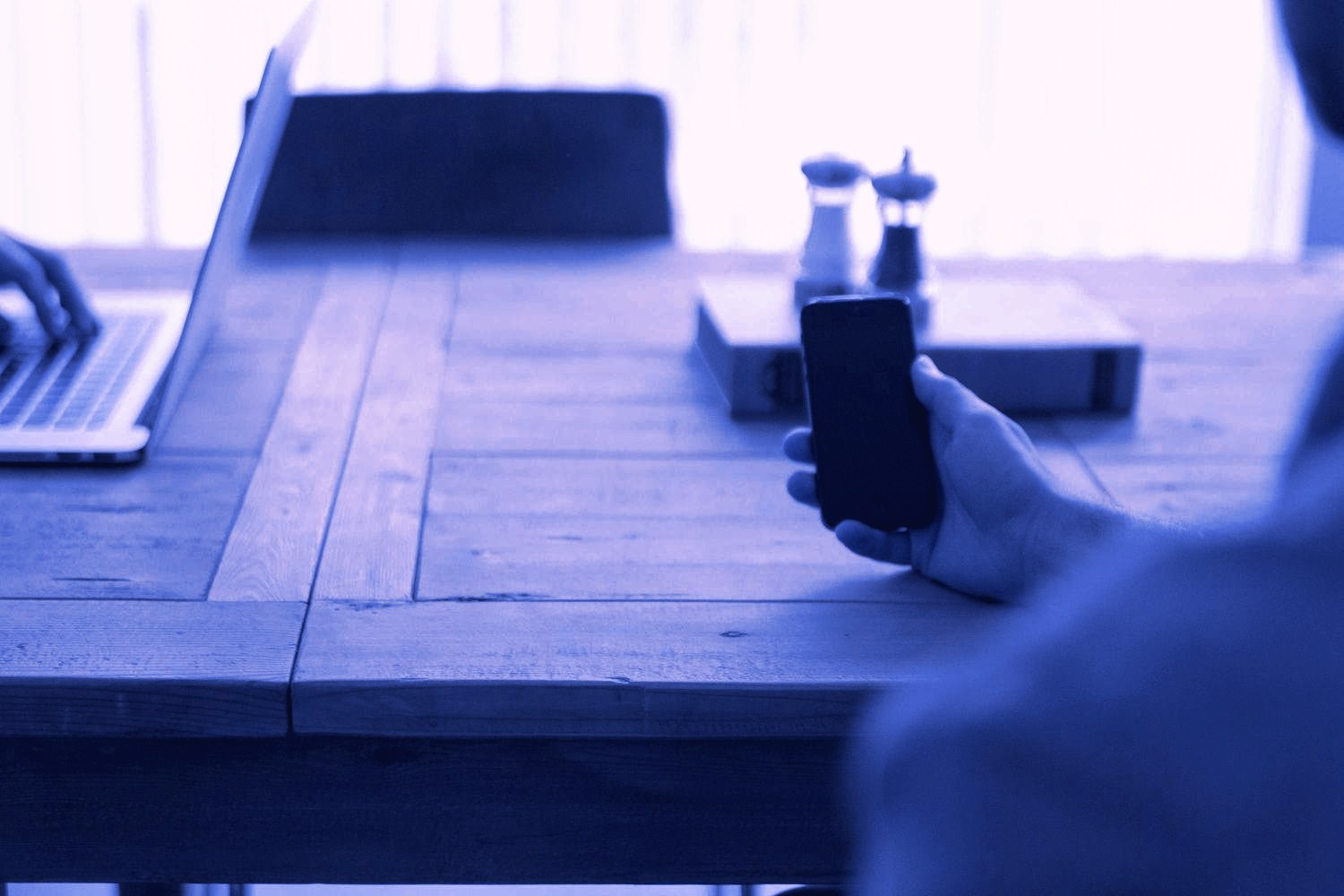A hand holding a phone beside a laptop, checking a lead in CRM & AI Automation at Devodin